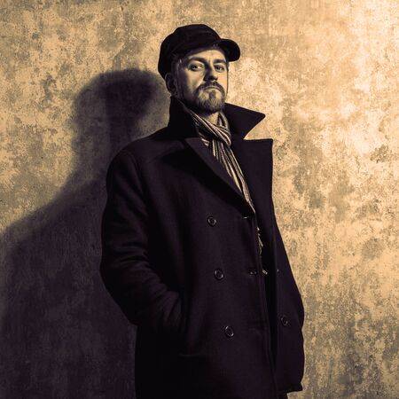 image of a caucasian man with grungy blond hair dressed warmly in a stylish black trench coat and a...