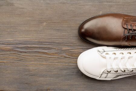 Men's classic brown shoes and white sneakers on a wooden background. Top view - image