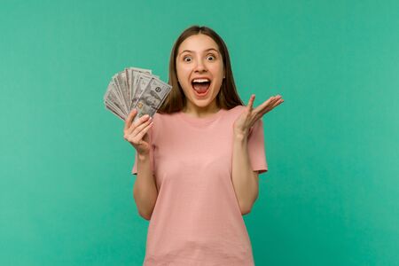 Portrait of a cheerful young woman holding money banknotes and celebrating isolated on blue backgroundの写真素材