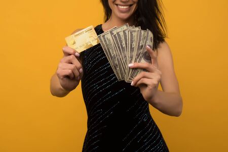 Photo of pleased happy young woman posing isolated over yellow wall background holding money and credit or debt card. - imageの写真素材