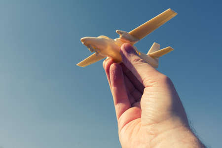 close up photo of male hand holding toy airplane against blue sky. image is retro filtered