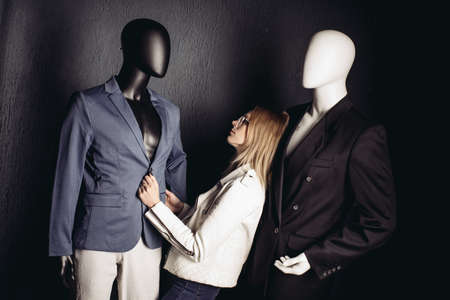 A young girl in glass suffers from loneliness in a society of stylish manikins on gray wall.の写真素材
