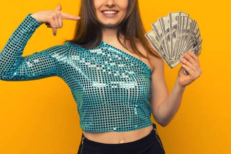 Joyful girl won the lottery and pointing on fan of US dollars in her hands on a yellow background - imageの写真素材