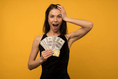 Photo of pleased happy young woman posing isolated over yellow wall background holding money and credit or debt card. - imageの写真素材