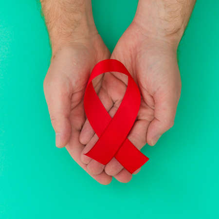 Healthcare and medicine concept - male hands holding red AIDS awareness ribbonの写真素材