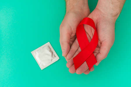 Healthcare and medicine concept AIDS awareness - male hands holding red ribbon and condom on blue backgroundの写真素材