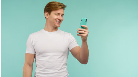 Handsome sporty red-haired guy pointing finger gold credit card on a blue background. - image