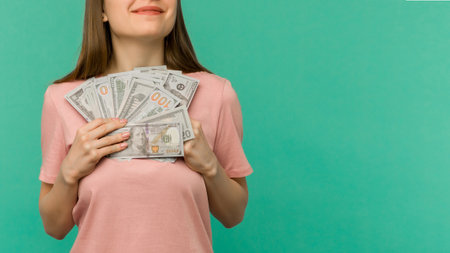 Portrait of a cheerful young woman holding money banknotes and celebrating isolated on blue backgroundの写真素材