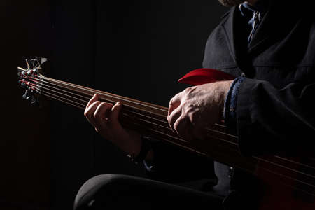 Male musician playing six-string fretless bass guitar on dark backgroundの写真素材