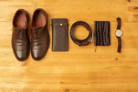 Men's accessories with brown leather wallet, belt, notebook, shoes and watch on wooden backgroundの写真素材