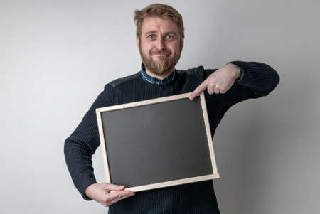 man with beard pointing on blank blackboard scared in shock with a surprise face, afraid and excited...