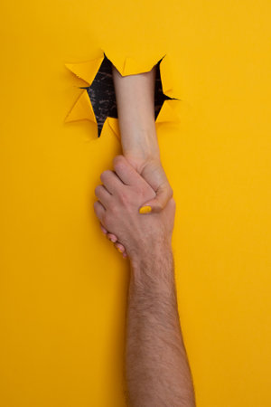 female hand shakes male from a hole in a torn yellow background. help conceptの写真素材
