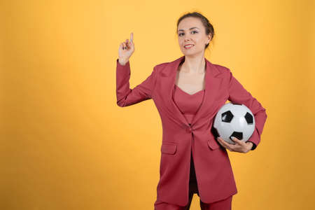 Beautiful young woman businesswoman with soccer ball posing on yellow background? Pointing finger upの写真素材