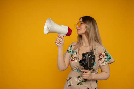 Beautiful young woman in yellow glasses posing with film camera and megaphone