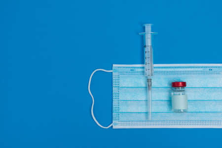 Syringe, mask, ampoules on a blue background, vaccination concept.