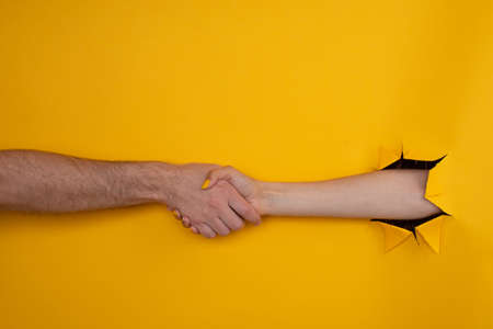 female hand shakes male from a hole in a torn yellow background. help conceptの写真素材