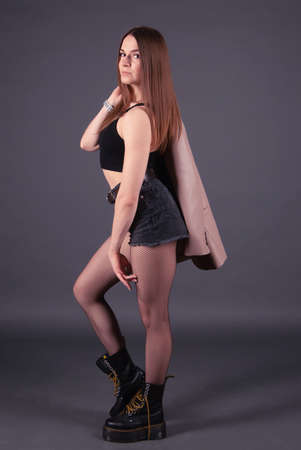 Portrait of a pretty girl wearing black jeans shorts and boots with brown leather jacket. full length standing pose on a studio backgroundの写真素材