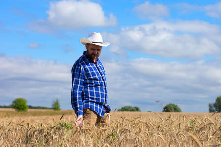 Man agronomist farmer in golden wheat field. Male holds ears of wheat in hand.の写真素材
