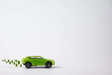 A toy green car rides over the background with an exhaust from birch leaves. The concept of reducing CO2 emissions from vehicles.の写真素材