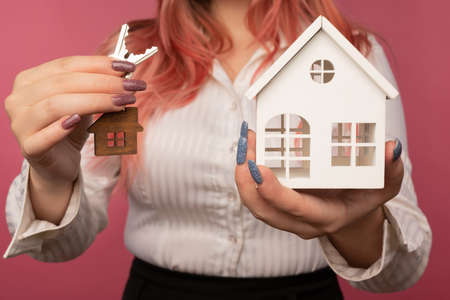 Beautiful female hands hold keys and a house on the backgroundの写真素材