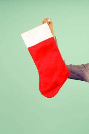 A beautiful sexy girl in a New Year's hat and gray dress points a finger at a Christmas sock....