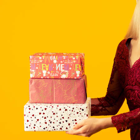 A beautiful asian girl in a red dress, hold in hands gifts on yellow background. Celebration of Christmas or new yearの写真素材