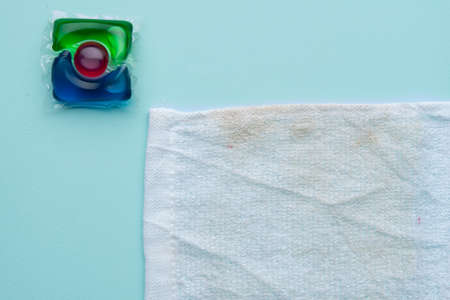 one water-soluble capsule for washing clothes and a dirty towel on a blue backgroundの写真素材