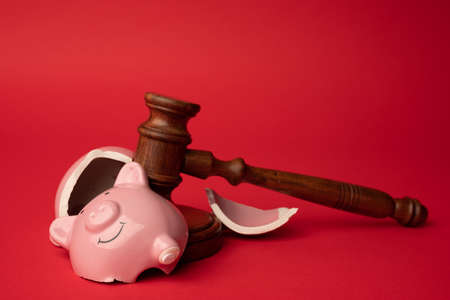 Broken pink piggy bank with wooden judge gavel on a red background. Law and bankruptcy conceptの写真素材