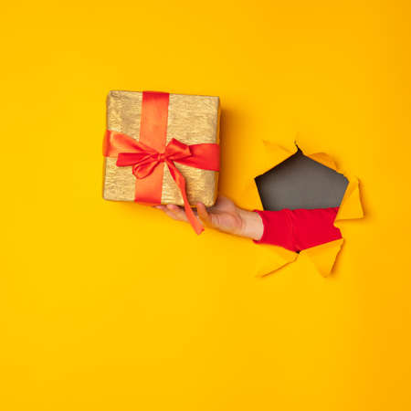 Santa's hand holding a box with a gift in the hole yellow backgroundの写真素材