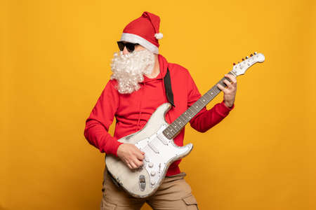Modern Santa Claus rock n roller play guitar emotionally isolated on yellow backgroundの写真素材