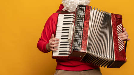 Modern Santa Claus play accordion emotionally isolated on yellow backgroundの写真素材