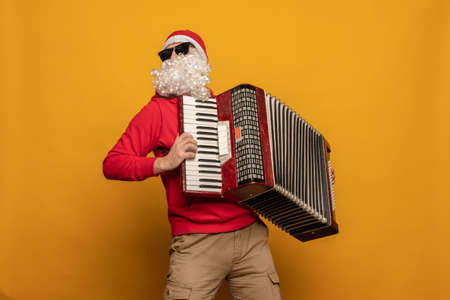 Modern Santa Claus play accordion emotionally isolated on yellow backgroundの写真素材