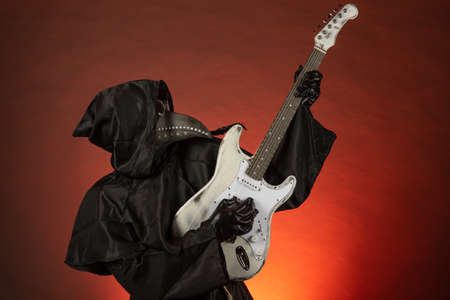 A man in a plague doctor costume plays the guitar emotionally on a red background