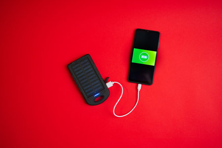 Modern smartphone charging clean energy solar battery powerbank top view on red backgroundの写真素材