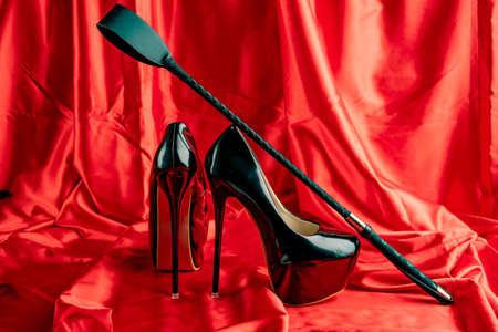 Adult sex games. BDSM items. Patent Fetish Extreme High Heel Stiletto Heels and whip on a red satin sheet.の写真素材