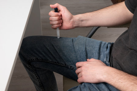 A man suffering from diabetes makes an injection of a syringe with a pen with insulin into his thigh through clothesの写真素材