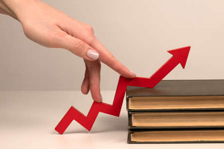 The fingers of a woman's hand step up the arrow of a chart lying on book. Knowledge investment and personal growth conceptの写真素材