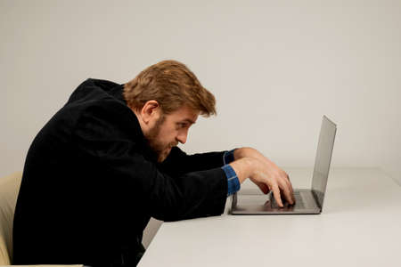 Beard emotional man in slouching position sitting in office room, working with laptopの写真素材