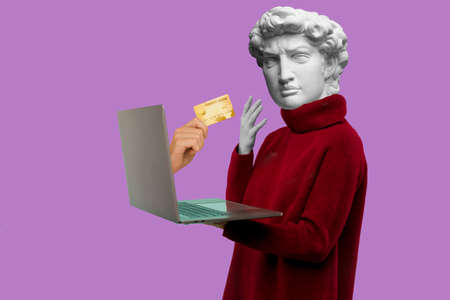 Abstract modern collage. The man with the plaster head of David in a red sweater looks at a laptop screen where does the hand with the credit card come out on a yellow backgroundの写真素材