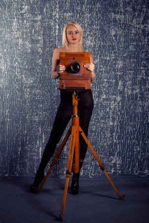 Adult slim blonde woman posing next to an old vintage wooden gimbal pavilion cameraの写真素材