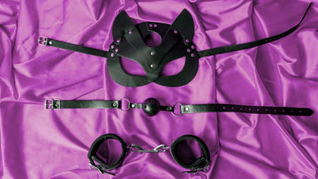adult sex games. BDSM items. Leather mask cat, gag ball, handcuffs on a purple satin sheet.の写真素材