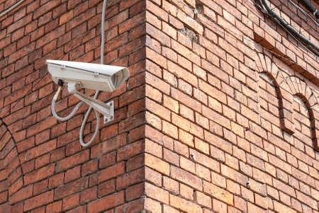 Closed-circuit television camera mounted on brick wall. CCTV security camera outdoors.の写真素材
