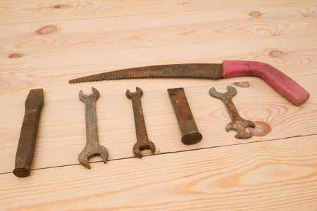 Rusty old open end wrenches, chisels, saw on a wooden background