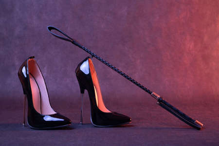Black shiny high heel shoes and a whip on a dark backgroundの写真素材