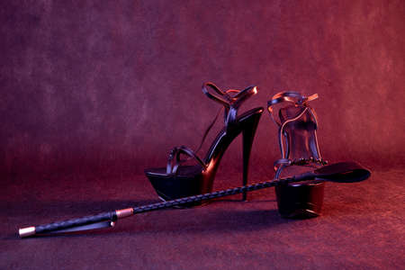 Black shiny high heel shoes and a whip on a dark background