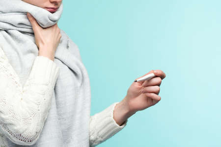 Young woman having flue taking thermometer against blue background. Beautiful lady is sick with a...