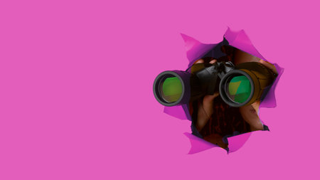 Female hand holds black binoculars on a pink background. Journey, find and search conceptの写真素材