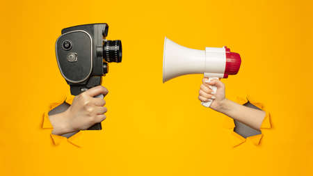 Woman holding megaphone and small video old retro black camera 8 mm in paper torn hole in yellow backgroundの写真素材