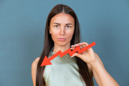 Sad businesswoman holds a red arrow chart pointing down. The concept of reducing costs and profits, falling living standards and prices. Decreased projections, depressed economies.の写真素材