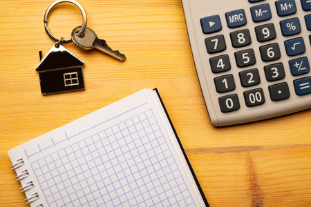 Buy or rent concept. Keys with trinket in shape of house and notepad with calculatoron on wooden background, top viewの写真素材
